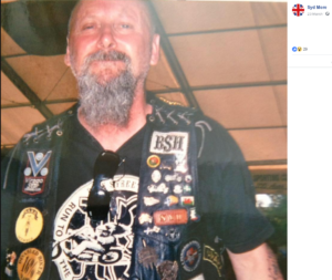 Syd More. He has a long grey beard and mustache. His hair is bald and he's wearing a biker jacket with patches
