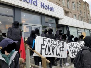 Antifascists stood in front of the Beresford Hotel. Dressed mostly in black, and holding banners "fascists fuck off" and "racists not welcome"