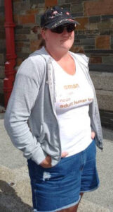 Woman wearing a dark cap, dark sunglasses, and a t-shirt with a dictionary definition of "woman" on it